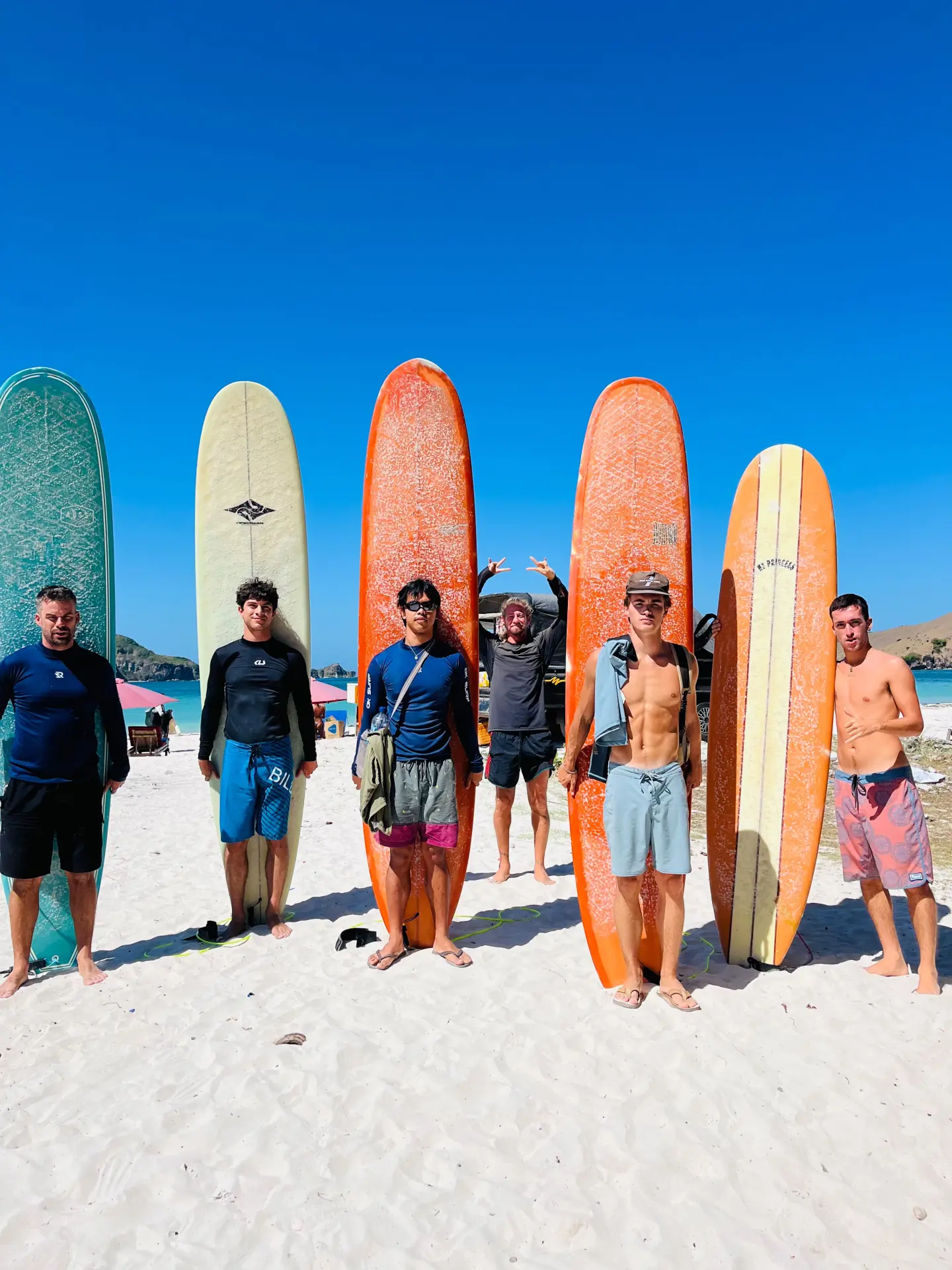 Surfers standing with colourful longboards on a sunny Lombok beach